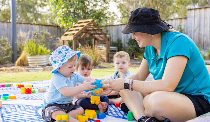 A St Nicholas Early Education educator with a child in St Nicholas' nursery program, playing outside with blocks