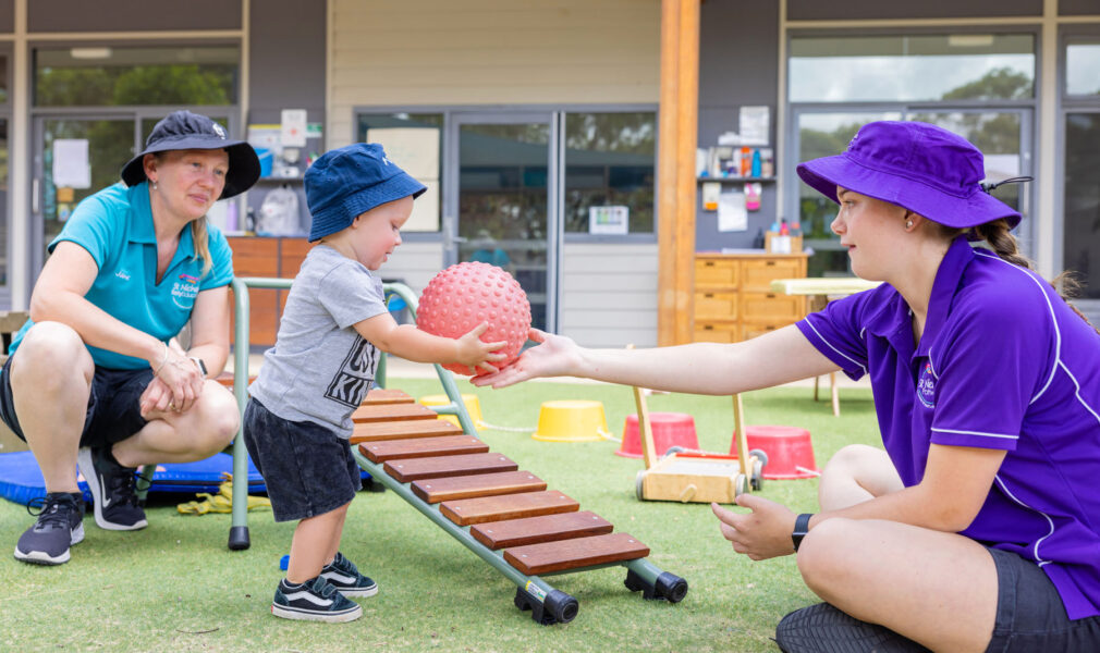 Child, school based trainee and educator playing with a ball at Branxton early education centre