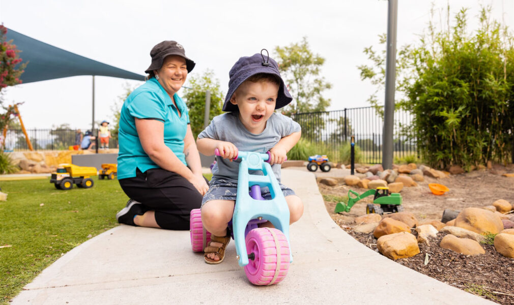 Child riding on bike supervised by educator outside at Muswellbrook early education centre