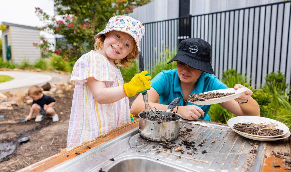 Child and educator playing in mud kitchen together outside at Muswellbrook early education centre