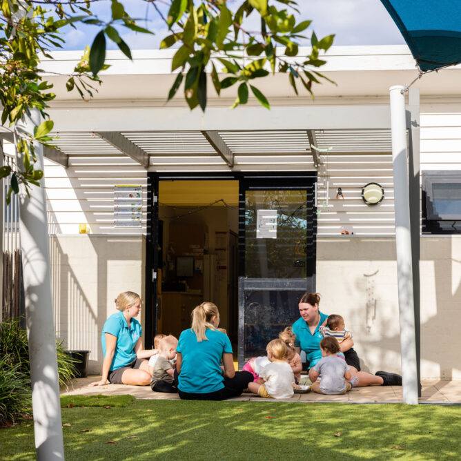 Educators and children sitting outside together at Newcastle West early education centre