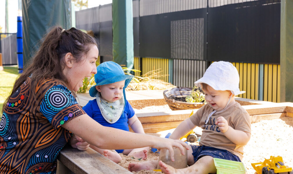 Educator and children in sandpit together outside at Raymond Terrace early education centre