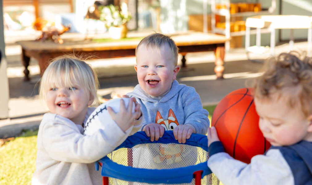 Children laughing and playing with basketball outside at Singleton early education centre