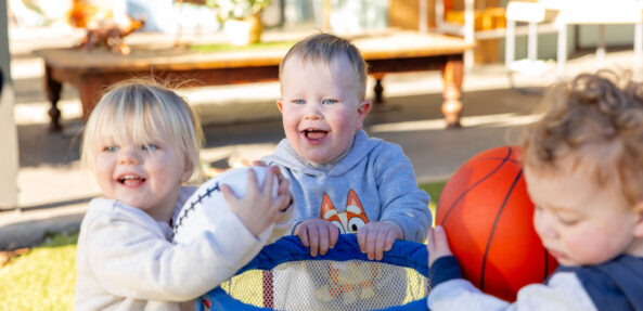 Children laughing and playing with basketball outside at Singleton early education centre