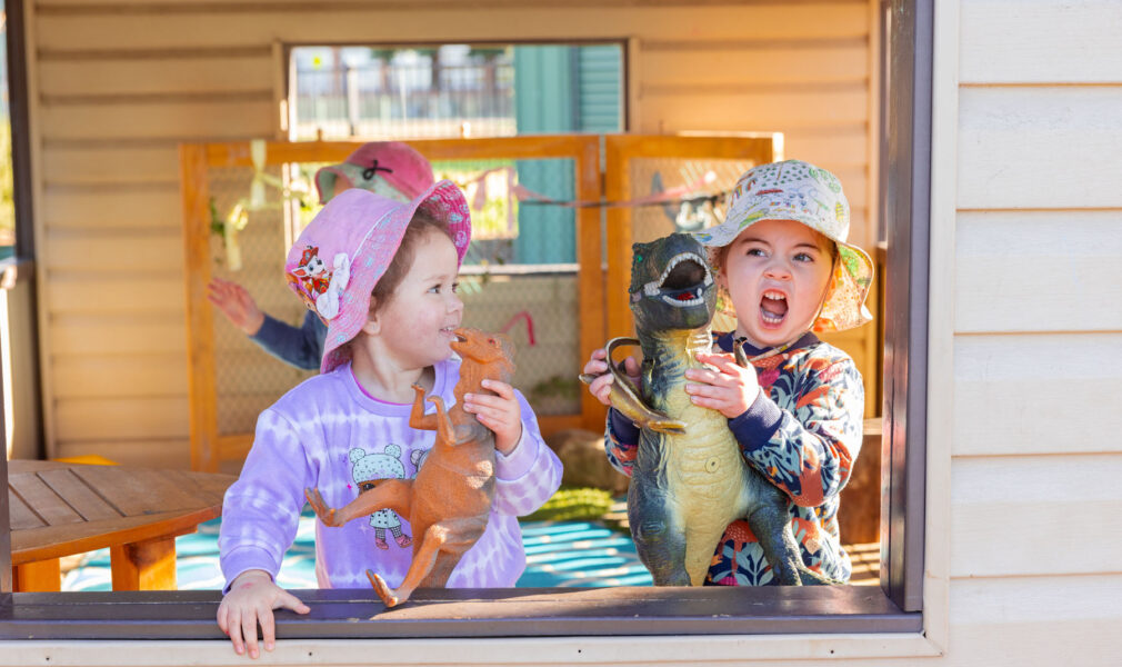 Children playing with dinosaurs together in cubby outside at Singleton early education centre