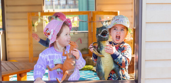 Children playing with dinosaurs together in cubby outside at Singleton early education centre