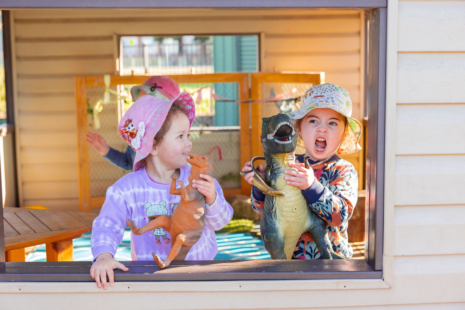 Children playing with dinosaurs together in cubby outside at Singleton early education centre