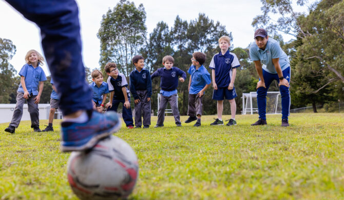 A St Nicholas OOSH educator playing soccer with children outdoors at one of the services