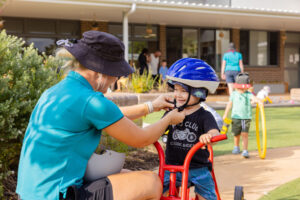 St Nicholas work-based trainee helping a child fasten their bike helmet at one of our early childhood centres