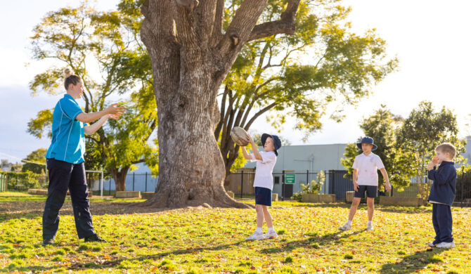 A St Nicholas OOSH Educator throwing and catching a ball with some children