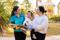 Child and parent on a centre tour with an educator in a teal shirt. Child is pointing to something in a floor book