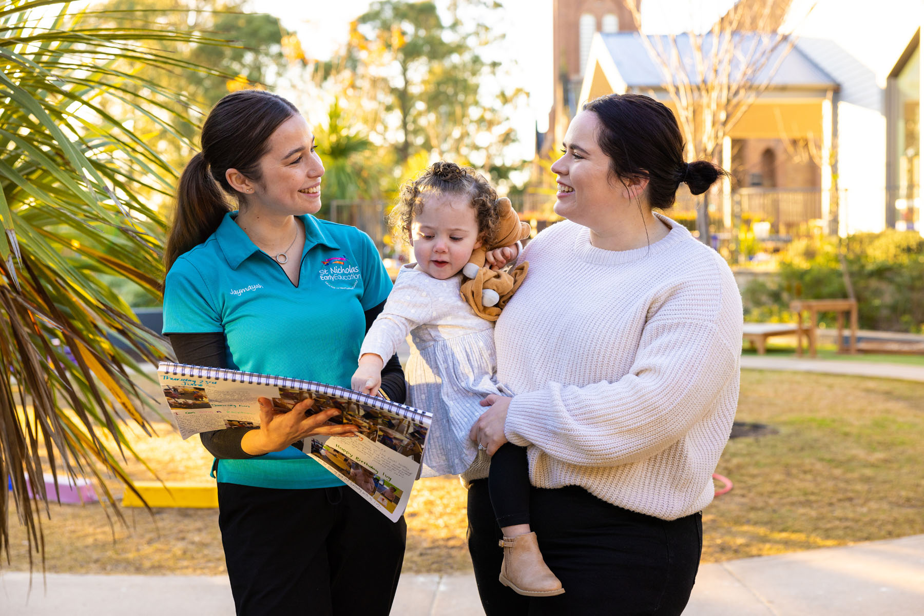 Child and parent on a centre tour with an educator in a teal shirt. Child is pointing to something in a floor book