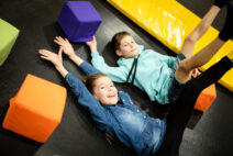 a boy and girl lying on a trampoline with their hands up