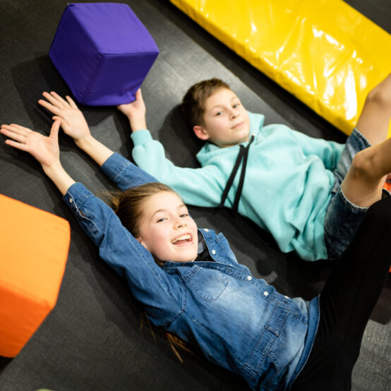 a boy and girl lying on a trampoline with their hands up