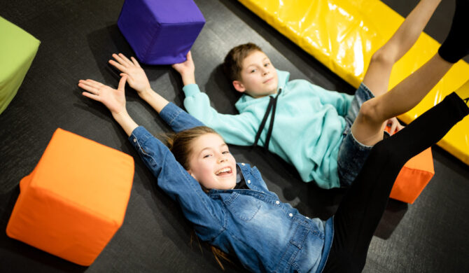 a boy and girl lying on a trampoline with their hands up